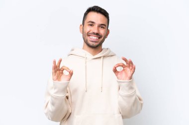 Beyaz arka planda izole edilmiş genç beyaz bir adam iki eliyle tamam işareti gösteriyor.