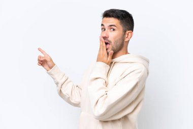 Beyaz arka planda izole edilmiş genç beyaz bir adam sürpriz bir ifadeyle işaret ederken...