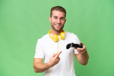 Genç yakışıklı bir adam yeşil krom arka planda izole edilmiş bir video oyunu kontrolörüyle oynuyor.