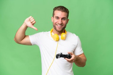 Yeşil krom arka planda izole edilmiş bir video oyunu kontrolörüyle oynayan yakışıklı genç adam gururlu ve kendinden memnun.