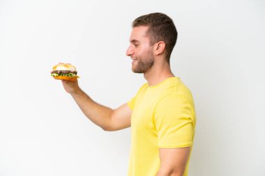 Beyaz arka planda mutlu bir ifadeyle izole edilmiş hamburger tutan genç beyaz bir adam.