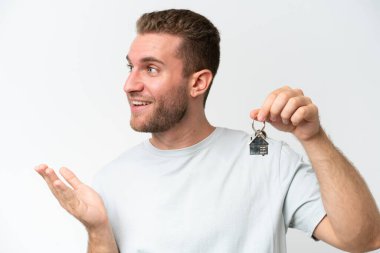 Beyaz arka planda yüzü sürpriz bir ifadeyle izole edilmiş ev anahtarlarını elinde tutan beyaz bir adam.