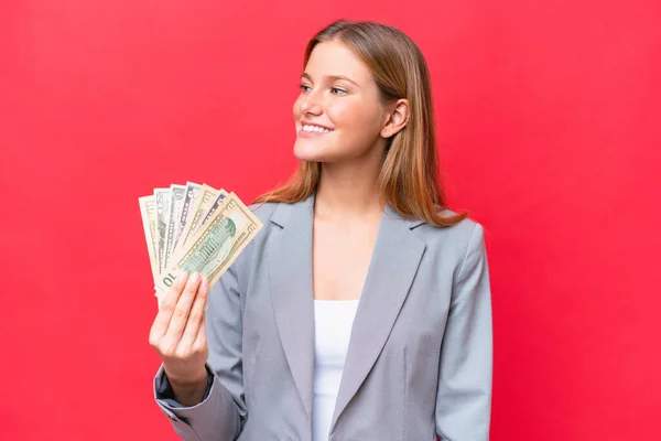 Νεαρή Γυναίκα Επιχειρηματίας Που Κρατάει Χρήματα Απομονωμένα Κόκκινο Φόντο Κοιτώντας — Φωτογραφία Αρχείου