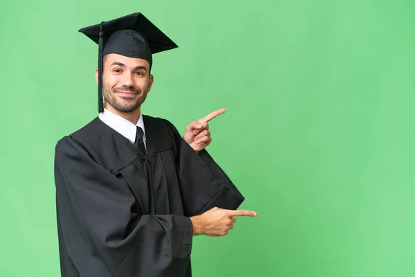Młody Absolwent Uniwersytetu Ponad Odosobnionym Tle Wskazując Palcem Bok Prezentując — Zdjęcie stockowe