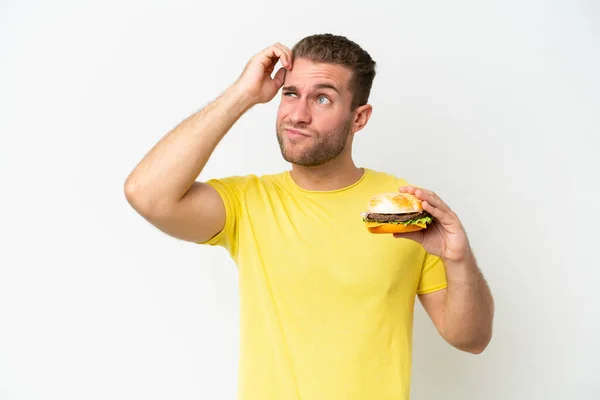 Młody Biały Mężczyzna Trzyma Hamburgera Odizolowany Białym Tle Mając Wątpliwości — Zdjęcie stockowe