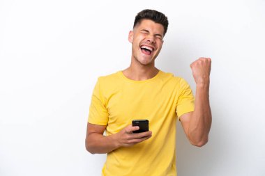 Beyaz arka planda izole edilmiş genç beyaz bir adam ve telefon zafer pozisyonunda.
