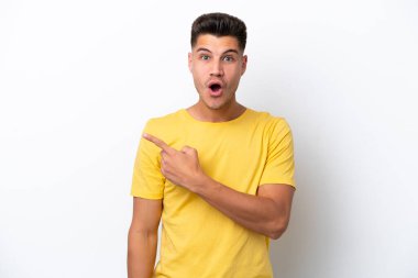 Beyaz arka planda izole edilmiş genç beyaz adam şaşırmış ve işaret ediyor.