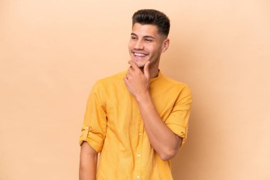 Beyazlı genç bir adam bej arka planda izole edilmiş, yana bakıyor ve gülümsüyor.