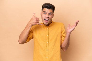 Beyazlı genç bir adam bej arka planda izole edilmiş telefon jestleri yapıyor ve şüpheli.