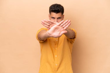 Young caucasian man isolated on beige background making stop gesture with her hand to stop an act