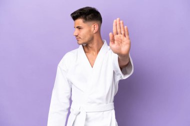 Mor arka planda karate yapan genç beyaz adam dur hareketi yapıyor ve hayal kırıklığına uğruyor.