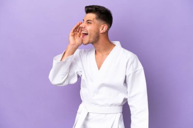 Mor arka planda karate yapan genç beyaz adam ağzı sonuna kadar açık bağırıyor.