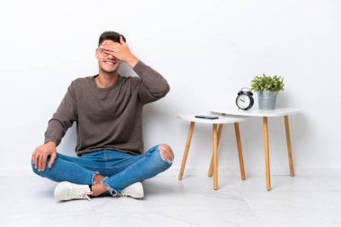 Evinde beyaz arka planda tek başına oturan beyaz tenli genç adam gözlerini elleriyle kapatıyor. Bir şey görmek istemiyorum.