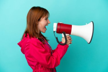 Redhead girl with medals isolated o blue background shouting through a megaphone