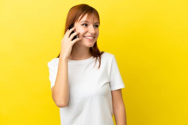 Sarı arka planda izole edilmiş kızıl saçlı bir kız cep telefonuyla sohbet ediyor.