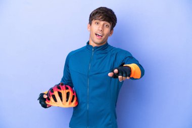 Mor arka planda izole edilmiş genç bir beyaz adam şaşırmış ve ön tarafı işaret ediyor.