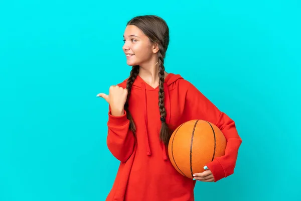 青い背景に孤立したバスケットボールをしている小さな白人の女の子は 製品を提示するために側面を指している — ストック写真