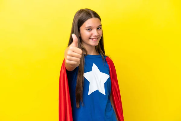 小さなCaucasianスーパーヒーロー女の子絶縁上の黄色の背景に親指アップとともに何か良いことが起こったので — ストック写真