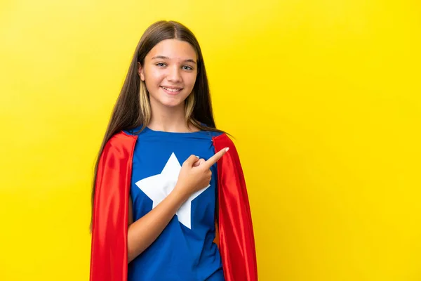 製品を提示する側を指して黄色の背景に隔離された小さな白人のスーパーヒーローの女の子 — ストック写真