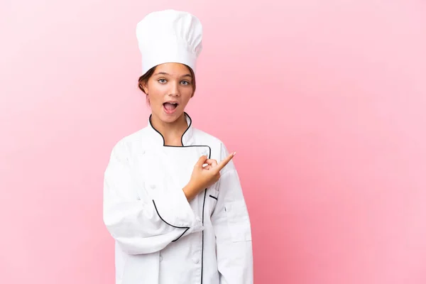 Pouco Caucasiano Chef Menina Isolado Fundo Rosa Surpreendido Apontando Lado — Fotografia de Stock