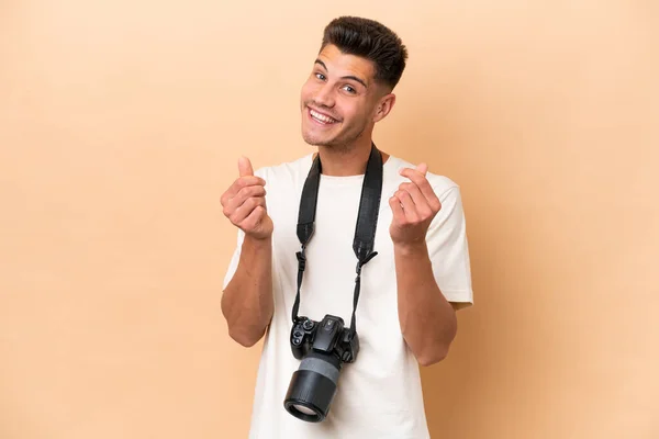 年轻的摄影师高加索人 由于米色背景而被隔离 做着赚钱的姿势 — 图库照片