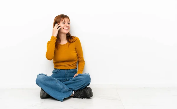 红头发姑娘坐在地板上 孤零零地坐在白色的背景上 和别人用手机交谈 — 图库照片