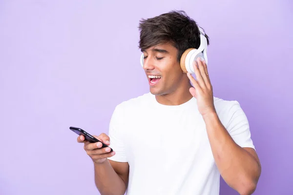 Νεαρός Καυκάσιος Άνδρας Απομονωμένος Μωβ Φόντο Ακούγοντας Μουσική Κινητό Και — Φωτογραφία Αρχείου