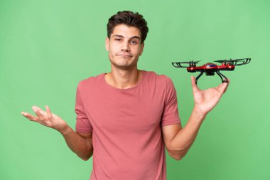 Kafkasyalı genç bir adam arka planda İHA tutuyor. Omuzlarını kaldırırken şüpheyle hareket ediyor.