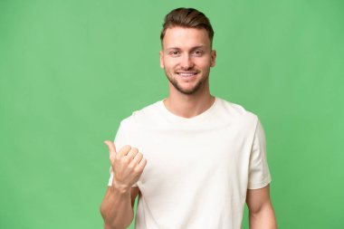 İzole edilmiş geçmişi olan genç sarışın beyaz bir adam bir ürünü sunmak için kenarı işaret ediyor.