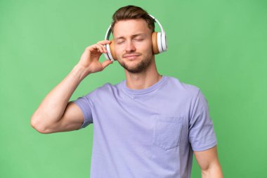 Sarışın, beyaz, soyutlanmış arka planda müzik dinleyip dans eden genç bir adam.