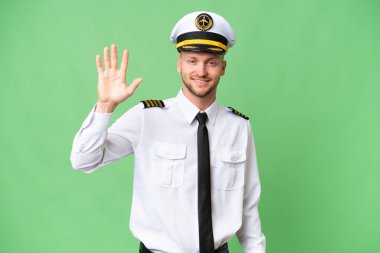 Uçak pilotu arka planda izole edilmiş, mutlu bir ifadeyle selamlıyor.