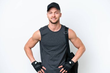 Spor çantalı genç sarışın beyaz adam izole edilmiş beyaz arka planda kolları kalçasında ve gülümsüyor.