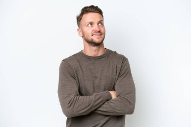 Beyaz arka planda izole edilmiş genç sarışın adam gülümserken yukarı bakıyor.