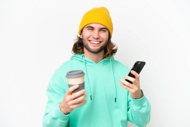 Beyaz krom arka planda izole edilmiş genç bir adam elinde kahve ve bir cep telefonu tutuyor.