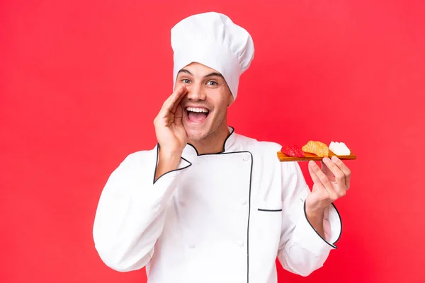 Joven Chef Caucásico Sosteniendo Sashimi Aislado Sobre Fondo Rojo Gritando — Foto de Stock