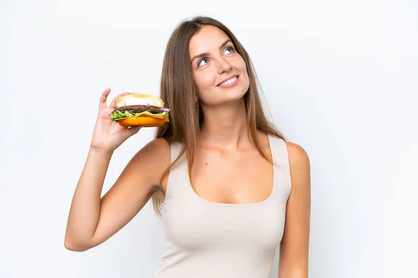 Młoda Ładna Kobieta Trzyma Hamburgera Odizolowany Białym Tle Patrząc Górę — Zdjęcie stockowe
