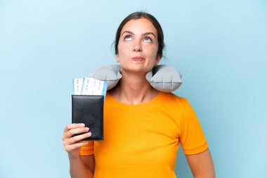 Şişirilebilir seyahat yastığı olan genç ve güzel bir kadın mavi arka planda izole edilmiş ve yukarı bakıyor.