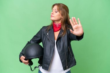 Motorsiklet kasklı orta yaşlı, beyaz bir kadın izole edilmiş arka planda durup jest yapıyor ve hayal kırıklığına uğruyor.