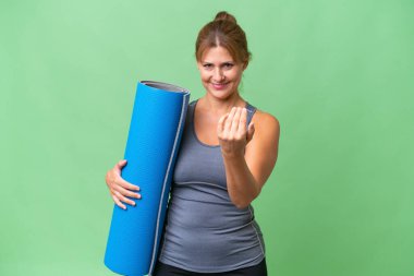 Orta yaşlı sporcu bir kadın yoga derslerine giderken arka planda bir paspas tutuyor ve kendini davet ettiriyor. Gelmene sevindim.