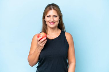 Orta yaşlı beyaz kadın, mavi arka planda elma ile izole edilmiş.