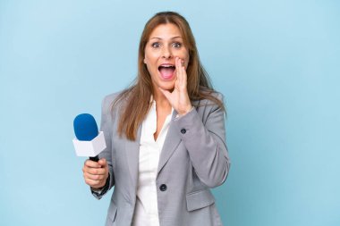 İzole edilmiş mavi arka planda, ağzı açık bir şekilde bağıran orta yaşlı televizyon sunucusu kadın.