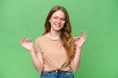 İzole edilmiş arka planda genç ve güzel bir kadın iki eliyle tamam işareti gösteriyor.