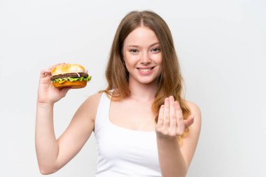 Beyaz arka planda izole edilmiş bir burger tutan genç ve güzel bir kadın, bizimle gelmesi için davet ediyor. Gelmene sevindim.