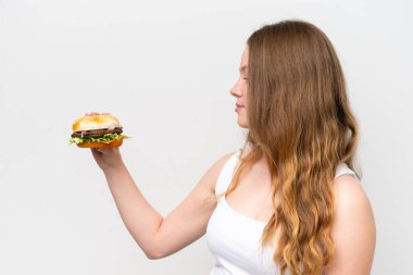 Genç, güzel bir kadın elinde hamburgerle beyaz arka planda mutlu bir ifadeyle.