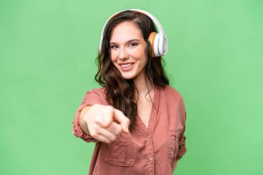 Kafkasyalı genç bir kadın izole edilmiş arka planda müzik dinliyor ve ön tarafı işaret ediyor.