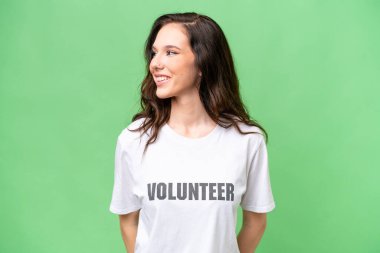 Genç gönüllü beyaz kadın izole edilmiş arka planda yan tarafa bakıyor ve gülümsüyor.