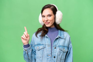 İzole edilmiş arka planda kışlık kuklalar takan genç beyaz kadın en iyinin işareti olarak parmağını kaldırıyor.