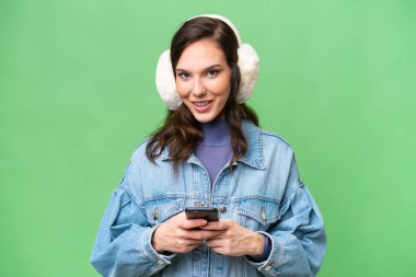 İzole edilmiş arka planda kışlık kuklalar takan genç beyaz kadın cep telefonuyla bir mesaj gönderiyor.