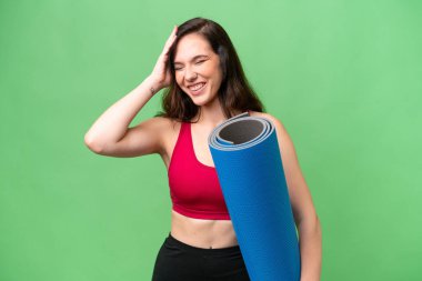 Genç sporcu kadın yoga derslerine giderken izole bir arka planda paspas tutuyor ve gülümsüyor.