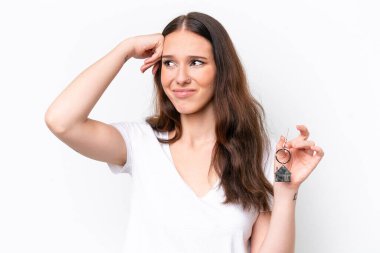 Beyaz arka planda izole edilmiş ev anahtarlarını elinde tutan genç beyaz bir kadın. Şüpheleri var ve kafası karışmış bir yüz ifadesi var.